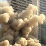Nuvem de poeira durante implosão de edifício em Brasília, alertando para riscos ambientais.