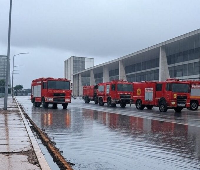 Rua alagada em Brasília com veículos de bombeiros do DF atendendo ocorrências de chuvas intensas, revelando falhas na infraestrutura.