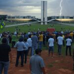 Manifestação em Brasília com tempestade e raios, simbolizando sobrevivência e exílio político.