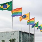 Fachada da Câmara Legislativa do DF em Brasília sob céu nublado, com bandeiras arco-íris, representando anúncio de programa com críticas ao apoio LGBTQIAPN+.