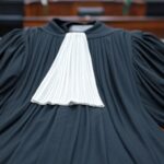 Toga de juiz vazia em tribunal brasileiro, com bandeiras a meio mastro, simbolizando luto pela morte de desembargador.