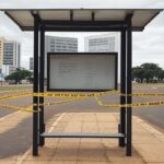Parada de ônibus vazia no DF com fita de isolamento policial, representando local onde corpo foi encontrado.