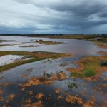 Transbordamento do Reservatório do Descoberto expondo riscos de inundações no Distrito Federal, com água invadindo margens e paisagem do planalto central.