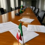 Sala de conferência em Brasília com bandeiras do Brasil e México, simbolizando debate sobre cooperação educacional e críticas à falta de transparência.