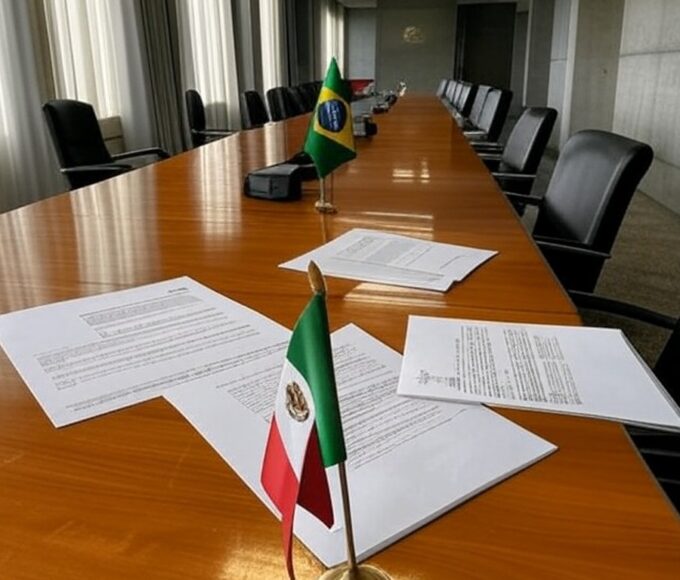 Sala de conferência em Brasília com bandeiras do Brasil e México, simbolizando debate sobre cooperação educacional e críticas à falta de transparência.