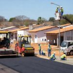 Obras de infraestrutura no Riacho Fundo II com máquinas pavimentando ruas e calçadas, investimento do GDF em melhorias urbanas.