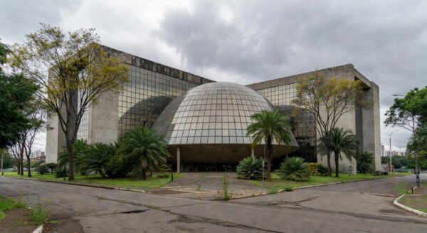 Fachada da Câmara Legislativa do DF em Brasília, com pódio vazio e prédios de seguros ao fundo, simbolizando homenagem criticada por ignorar crises.