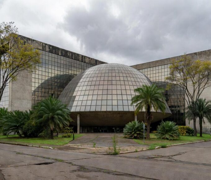 Fachada da Câmara Legislativa do DF em Brasília, com pódio vazio e prédios de seguros ao fundo, simbolizando homenagem criticada por ignorar crises.