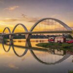 Ponte JK em Brasília sobre o Lago Paranoá com veículos de bombeiros, em estilo fotojornalístico.