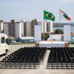 Ônibus do QualificaDF Móvel em praça de Paranoá durante formatura de alunos, com bandeiras e palco vazio.