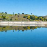 Reservatório de água no DF atingindo capacidade máxima, garantindo abastecimento hídrico, com barragem e paisagem natural.